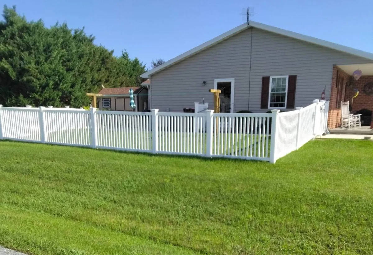 White picket-style fence with decorative post caps enclosing the lawn beside a house