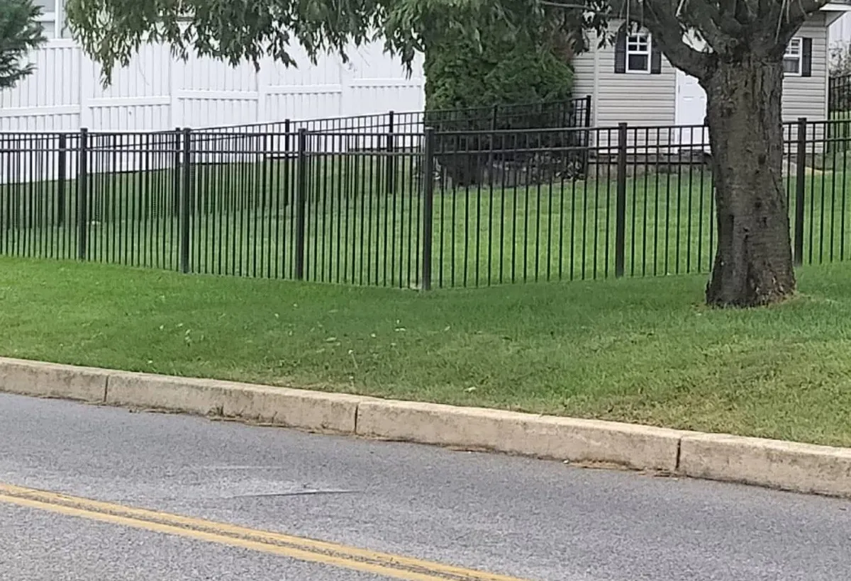 Black ornamental fence with vertical bars stepping along a residential lawn beside a curb