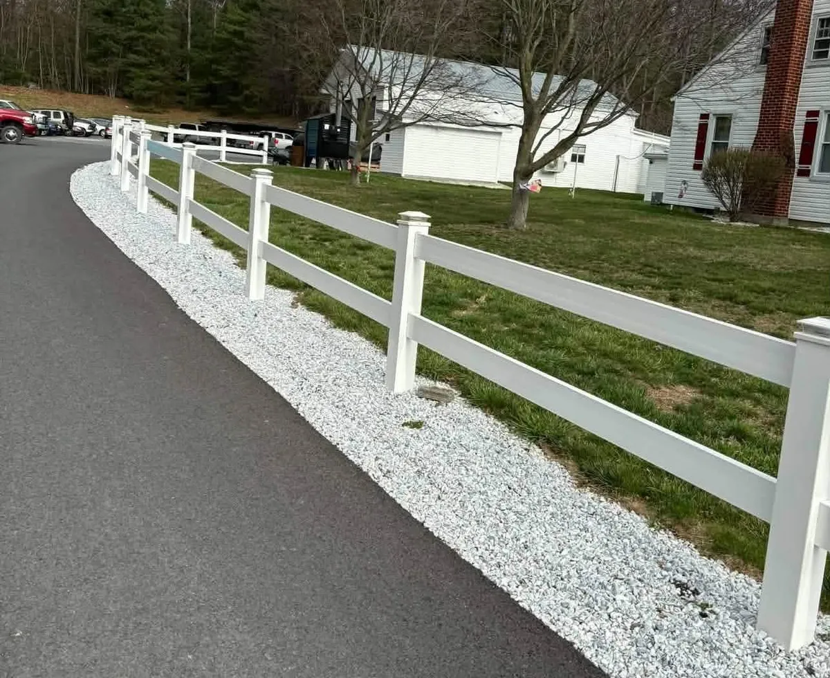 White rail fence curving along a paved drive with a white gravel border beside it