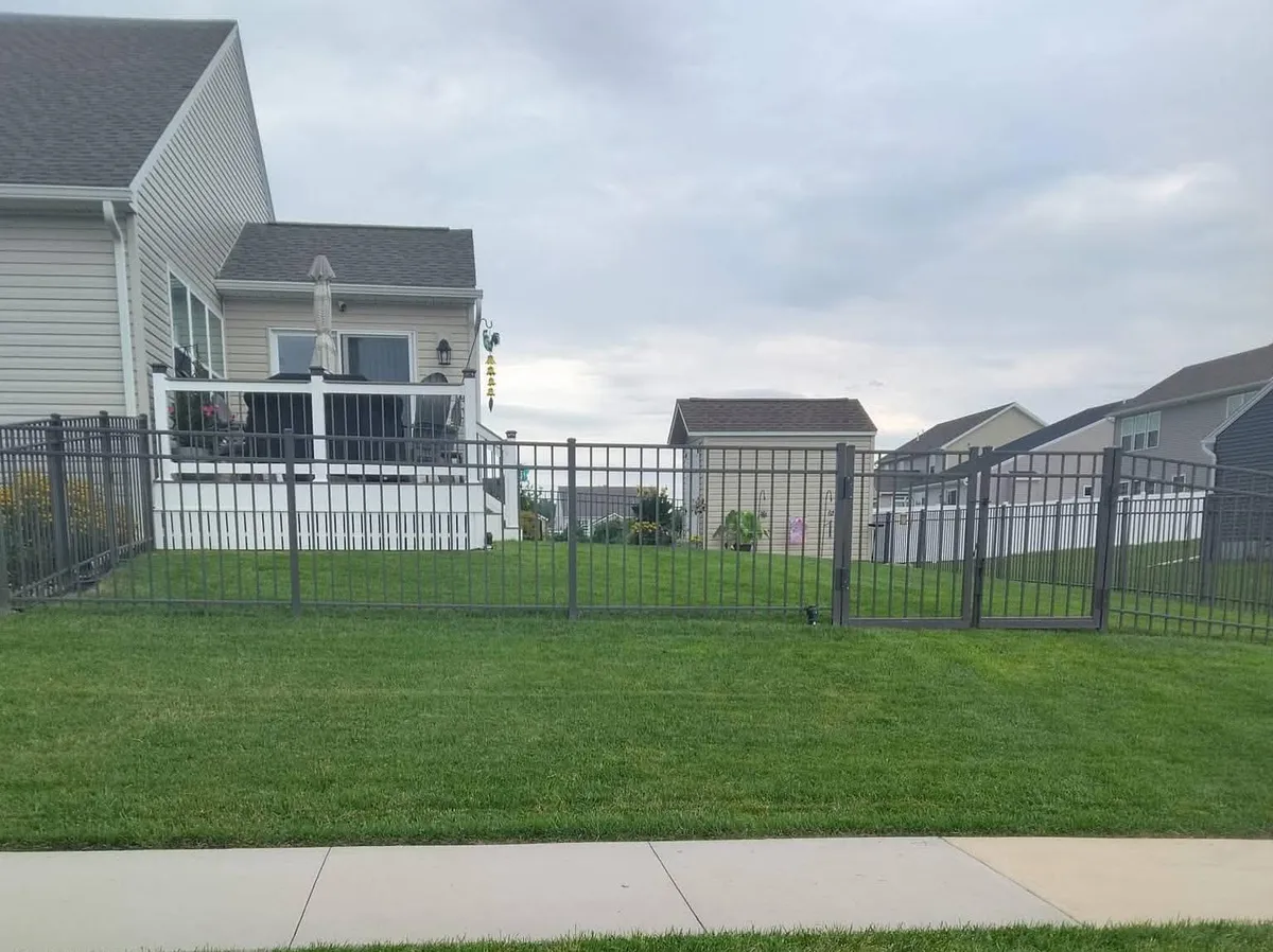 Dark ornamental fence with a double gate enclosing a backyard behind a sidewalk