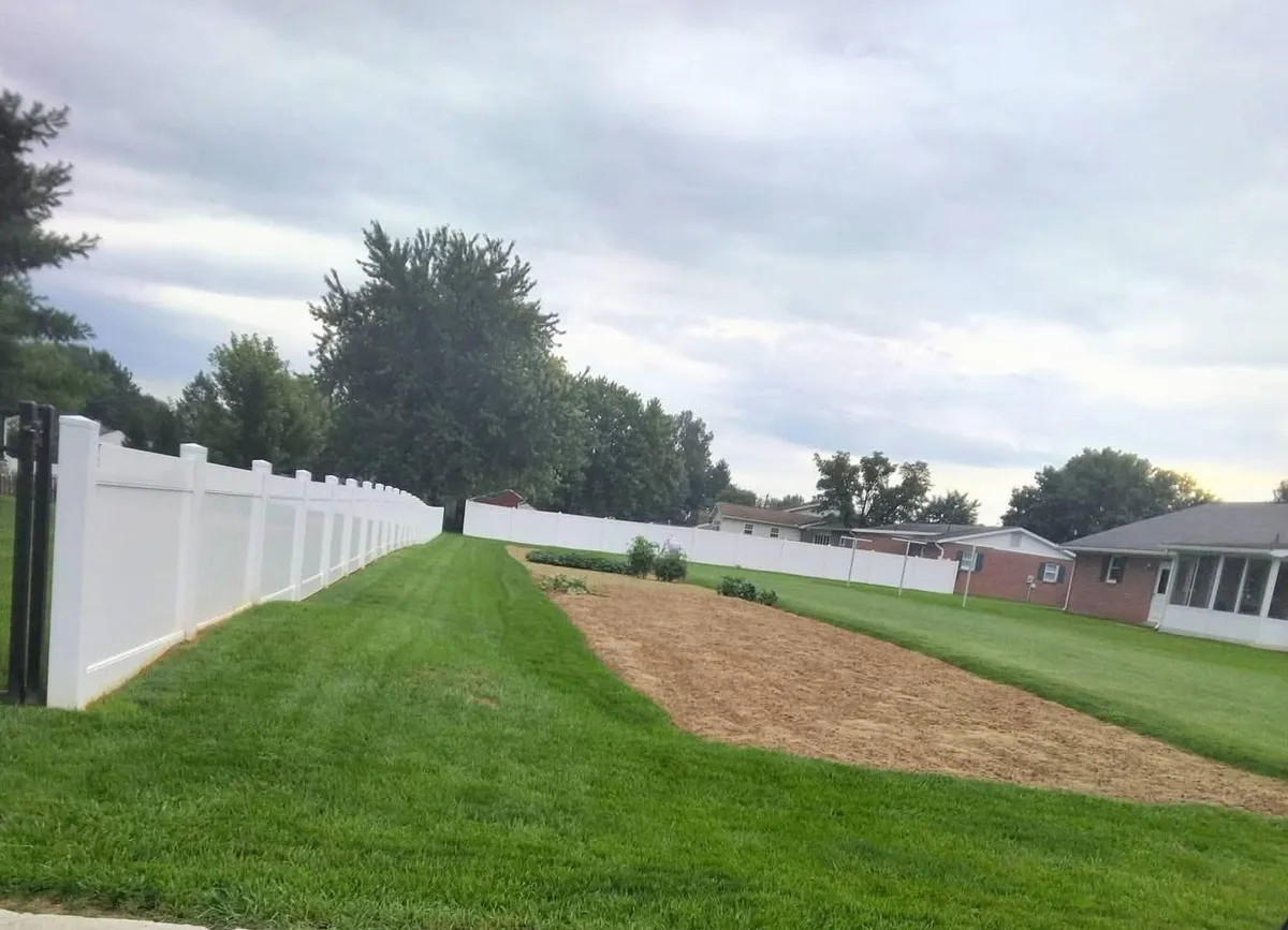 White solid-panel privacy fence running along a mowed lawn beside a garden plot